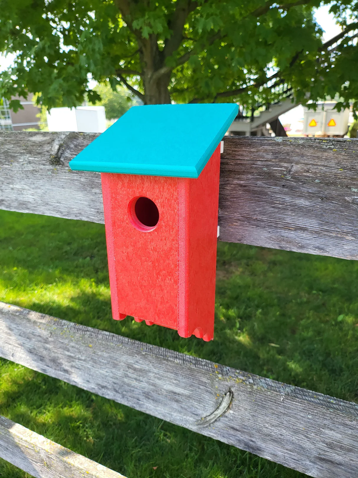 Vibrant red and turquoise handmade bird house mounted on a wooden fence, ideal for bluebirds and made from weather-resistant poly lumber.