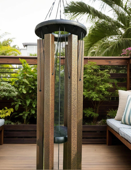 Unique windchimes featuring textured bronze aluminum tubes, black top ring, and deep resonating design, displayed on wooden deck with tropical garden backdrop for outdoor meditation and sound healing