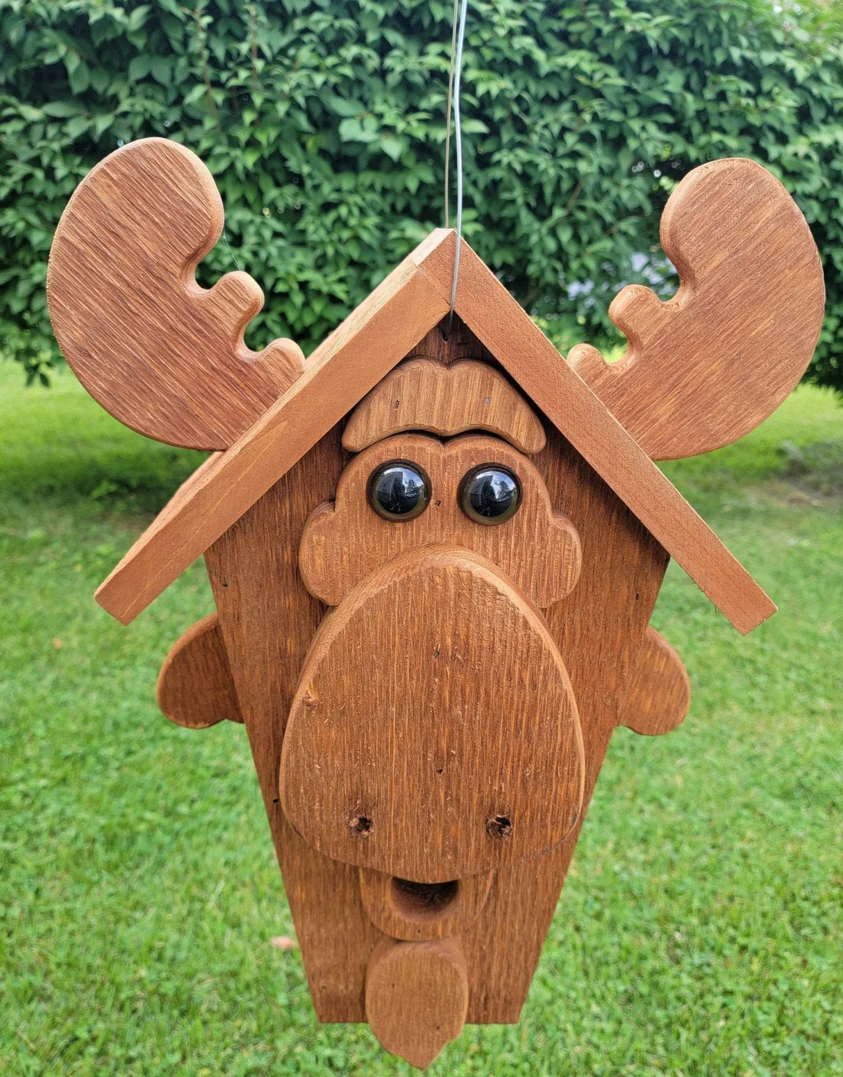 Handcrafted wooden birdhouse shaped like a moose face with antlers, hanging outdoors