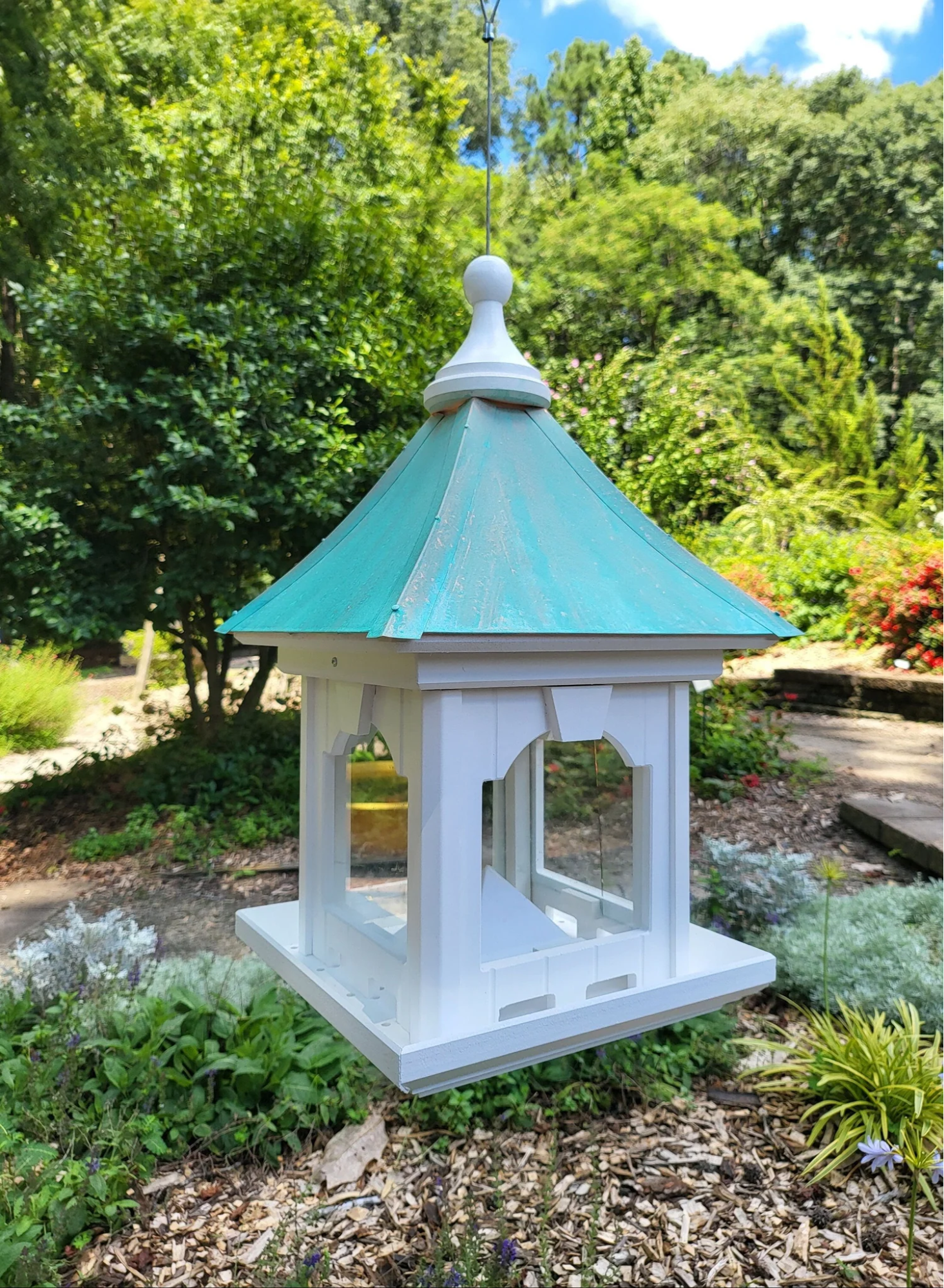 "Hanging bird feeder with a patina copper roof, white wooden frame, and large capacity feed tray, suspended in a garden setting."