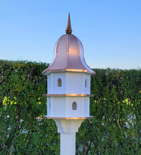 "Two-story white bird house with a copper roof, featuring eight nesting compartments and an elegant spire, mounted on a garden post."