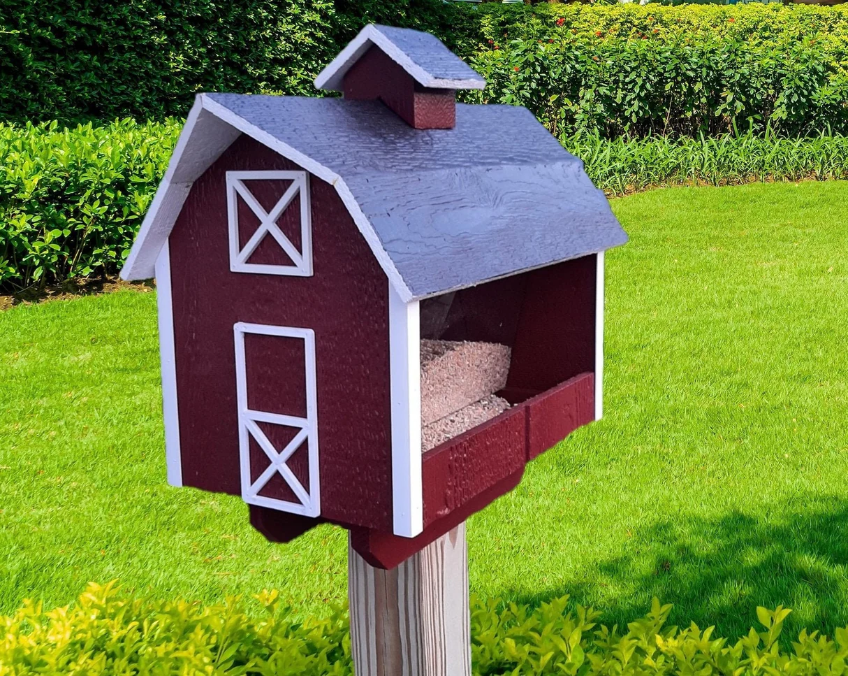 Red bird feeder shaped like a traditional barn with white trim, mounted in a well-manicured lawn