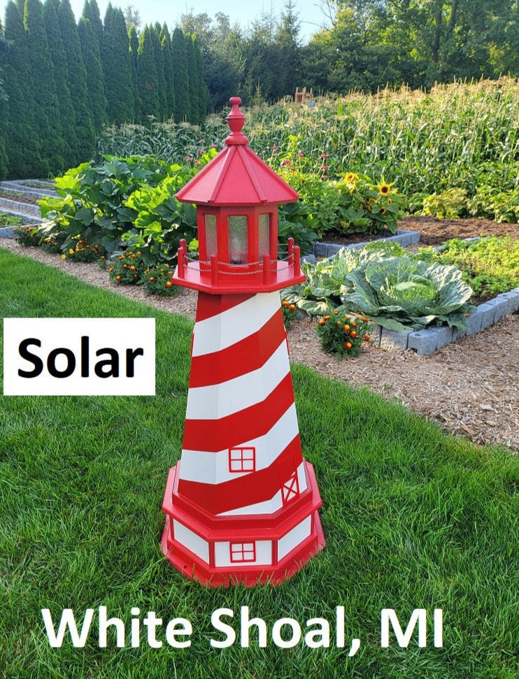 May include: A red and white striped lighthouse with a solar light. The lighthouse is in a garden setting with green grass and plants. The text &#39;Solar&#39; and &#39;White Shoal, MI&#39; are visible in the image.